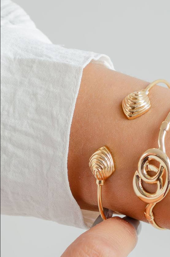 Gold bracelet on a wrist against a neutral background